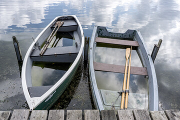 two small row boats full of water on a lake 