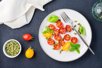 Sun-dried tomatoes with basil, sesame seeds and pumpkin on a plate on a black background. Vegetarian food. Top view