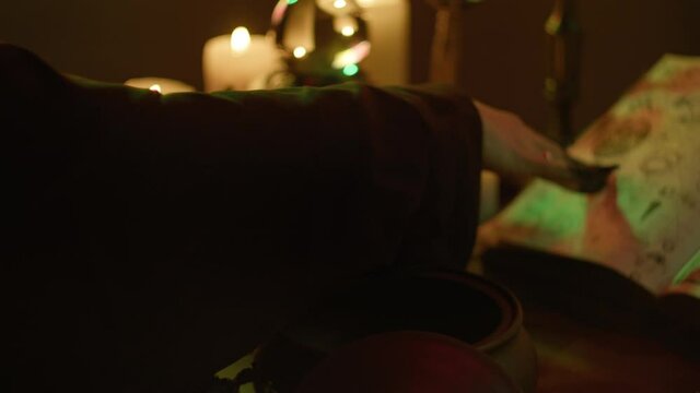 Witch cooking potion elixir close-up. Table with spellbook for making rite. Herbs, burning candles, crystal magic ball for sacrifice. Halloween theme, full moon, witchcraft. 