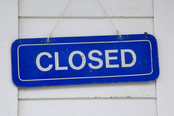Closed sign. White letters on blue background on white clapboard wall, 
