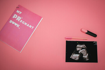 Ultrasound image of a baby, markers and pregnant book on a pink background. Flat-lay, top view with place for your text. Medical trends and concept.