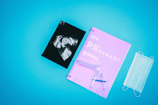 Vaginal speculum, medical mask, ultrasound picture of a child and pregnant book on a light blue background. Flat-lay, top view with place for your text. Medical trends and concept.
