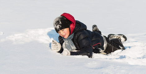 Fototapeta na wymiar A little boy plays in the snow in winter