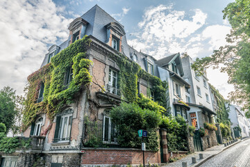 Immeuble bourgeois recouvert de végétation dans une rue pavée sur les pentes de Montmartre à...