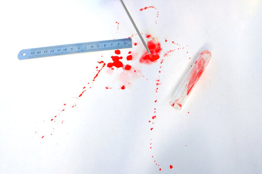 fresh splatter of red blood on white table from crime scene, measuring ruler, blood sample collection tube, forensic medical examiner work concept, police laboratory