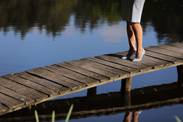 cropped photo of female legs walking on a wooden pier on the river