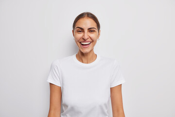 Portrait of happy European woman with gentle smile smiles joyfully dressed in casual t shirt isolated over white background. Carefree cheerful female model feels upbeat expresses sincere emotions