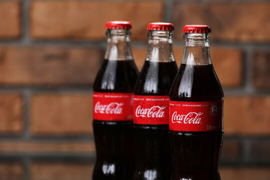 RIVNE, UKRAINE JUNE 26 2020: three Classic glass bottles Of Coca-Cola on brick wall background. cans of coca-cola