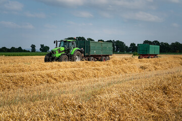 Getreideernte - am Feldrand wartet ein Schlepper mit Transportanhänger auf die Entladung des Mähdreschers.