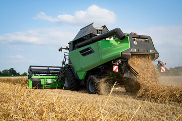 Obraz premium Getreideernte - Moderner Mähdrescher bei trockenem Erntewetter auf dem Feld im Einsatz.