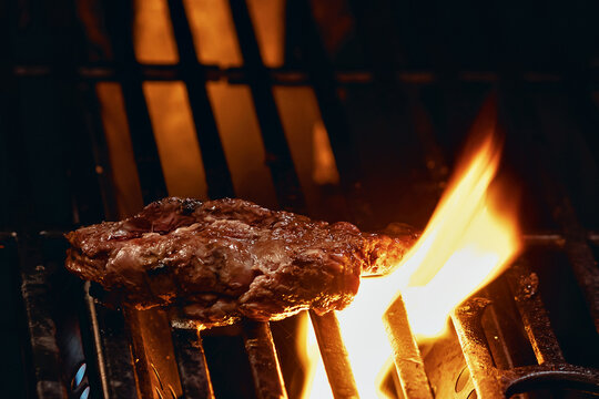 peda&ccedil;o de carne assando na grelha de uma churrasqueira com labaredas subindo 