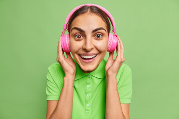 Good looking positive woman puts on wireless headphones listens favorite audio track smiles...