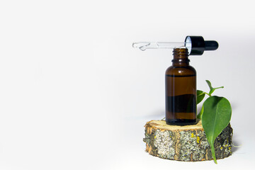 One glass bottle of brown serum with a dropper on a moss-covered wooden podium. Spa cosmetic concept. Place for your text. Organic cosmetics.