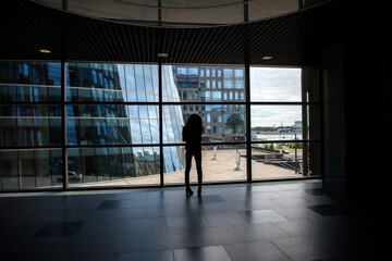 Fototapeta na wymiar A girl at the window with a view of skyscrapers. The concept of loneliness in a big city.