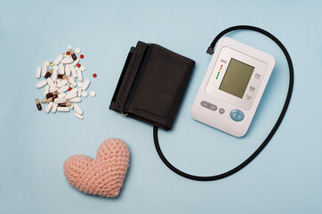 A device for measuring pressure, tonometer on a blue medical background, knitted heart and pills....