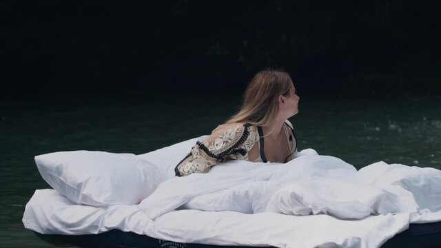 A sleeping girl wakes up in a beautiful place on an inflatable bed with a stunning view of nature and a waterfall