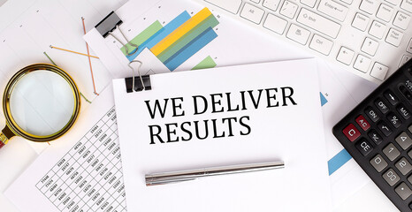 Obraz premium WE DELIVER RESULTS text on the white paper on the light background with charts paper ,keyboard and calculator