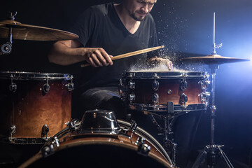 A male drummer plays snare drum with drumsticks in a dark room.