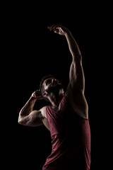 Side lit muscular Caucasian man silhouette. Athlete in red shirt posing against black background.