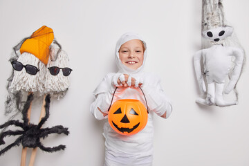 Happy small halloween child plays trick or treat jack o lantern pumpkin wrapped in white fabric...