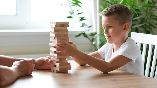 Father and son playing wooden block removal tower game at home together. Board game Jenga. Kids leisure concept.