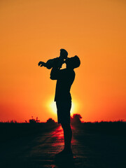 Fototapeta premium The silhouette of the father holds and kisses his child at sunset