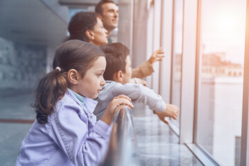 Family with two little kids looking through a window while waiting for their flight at the airport terminal