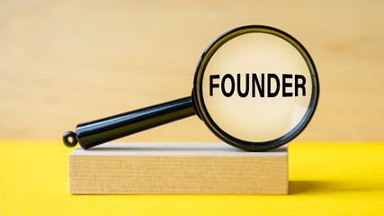 founder word through magnifying glass on wooden background