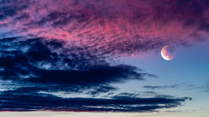 Particularly red-blue colorful sky photograph with a full moon made red by the setting sun at sunset. Full frame photograph.