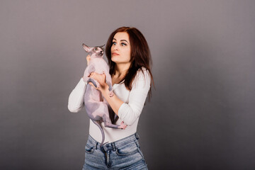 Young woman with canadian sphynx cat in studio, grey background