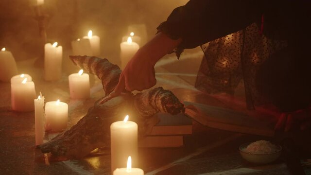 Crazy witch woman making fingerprint with blood on cow skull, sitting in pentagram circle. Evil sorceress doing rite and sacrifices at night, using black witchcraft, candles on floor. Halloween time.