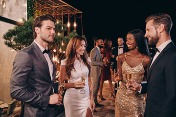 Group of people in formalwear communicating and smiling while spending time on luxury party