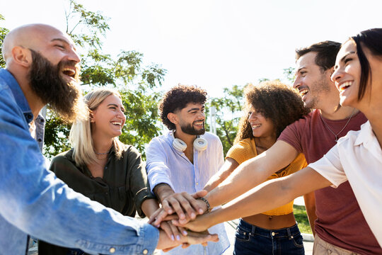 Group of united multiracial people stacking hands together - Cooperation, collaboration, community and unity concept with multiethnic young college students celebrating together on campus university