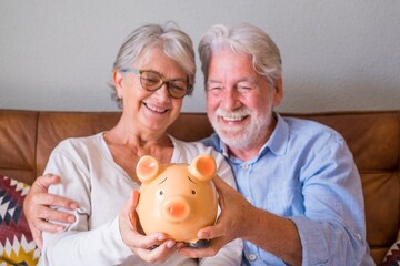 Close up of senior couple showing piggy bank to save money. Elderly couple holding piggy bank for...