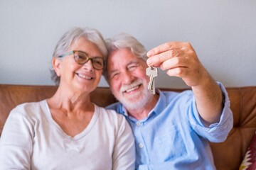 Close up of senior couple showing keys of house. Elderly couple holding keys for investment of...