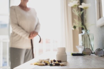 Assorted multicolored tablets, pills, capsules with bottle on table while senior woman standing in...