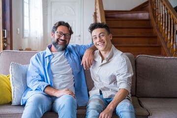 Happy father and son sitting on sofa at home. Cheerful father with teenage son sitting on couch in...