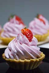 Mouthwatering array of petite dessert tarts, each crowned with velvety pink cream and a ripe strawberry, capturing culinary delight.