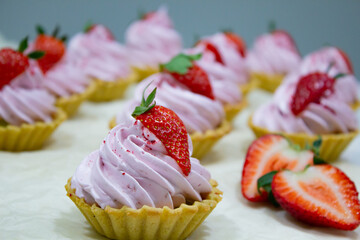 Elegant lineup of mini tarts with velvety pink frosting, garnished with strawberries, set against a neutral backdrop.