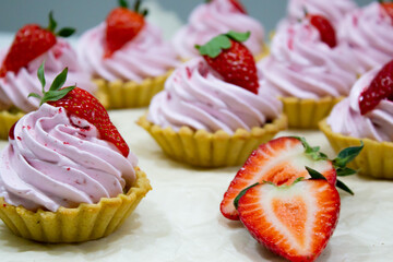 Lush pastel pink tartlets crowned with strawberries, displayed with a halved berry, symbolizing sweet sophistication.