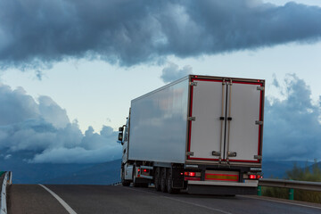 Truck with refrigerated semi-trailer circulating in a change of slope and with a cloudy sky.