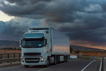 Truck with refrigerated semi-trailer driving on a day with storm clouds.
