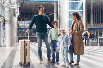 Full length of family with two little kids waiting for their flight at the airport terminal