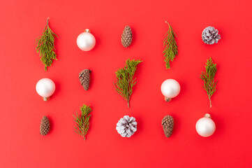 Christmas background. Minimalistic composition. On a red background, miniature coniferous branches, cones, Christmas balls. Abstraction. Interior decor.