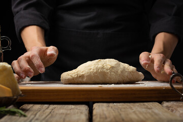A chef in a black uniform kneads dough on a wooden cutting board. Macro photography. Minimalism. Wooden texture. Country style. cooking pie, pizza, cake, bread, pasta.