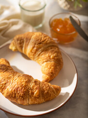 Two mouth-watering croissants on a white plate, amber orange jam and a glass of milk in the background. White background. Pastel shades. Advertising, menu design.