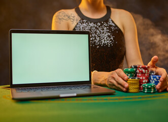 A woman plays poker in an online casino. On the table is an open laptop and many stacks of multi-colored chips. Gambling, online casino, strategy games.