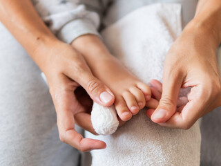 Mother bandages her child's big toe. Close-up photo of kid's foot with bandaged finger. First aid in case of small domestic injury.