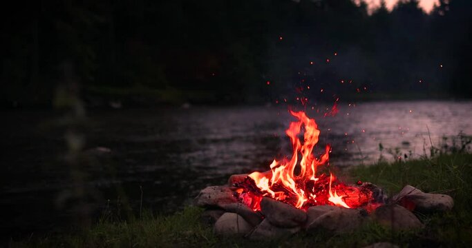 dancing sparks of a campfire flame near the river. Forest on the background. Travelling and camping concept