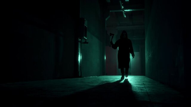 Maniac walking with axe in dark corridor. Mystical scary murderer going to kill, carrying murderous weapon. Halloween costume of killer. Horror scene or nightmare concept. 